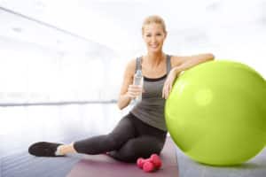 smiling woman sitting next to fitness ball and holding a bottle of water