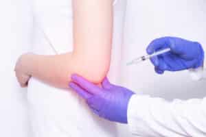 Doctor injects Corticosteroid to a young girl in a sore elbow joint