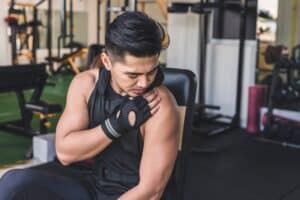 Man at gym touching shoulder with new pain that could be a SLAP tear