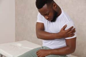 Man holding his shoulder in discomfort, representing shoulder pain when lifting or moving the arm.